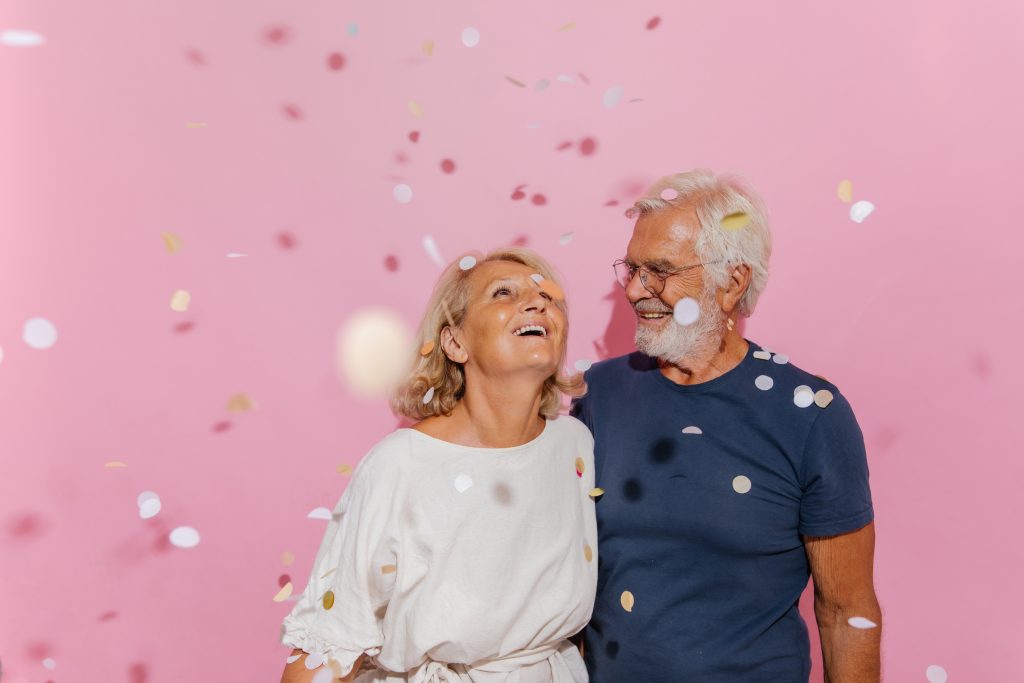 elderly couple with confetti on pink background