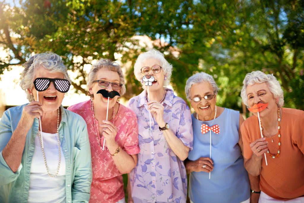 Group of senior women smiling while using funny masks