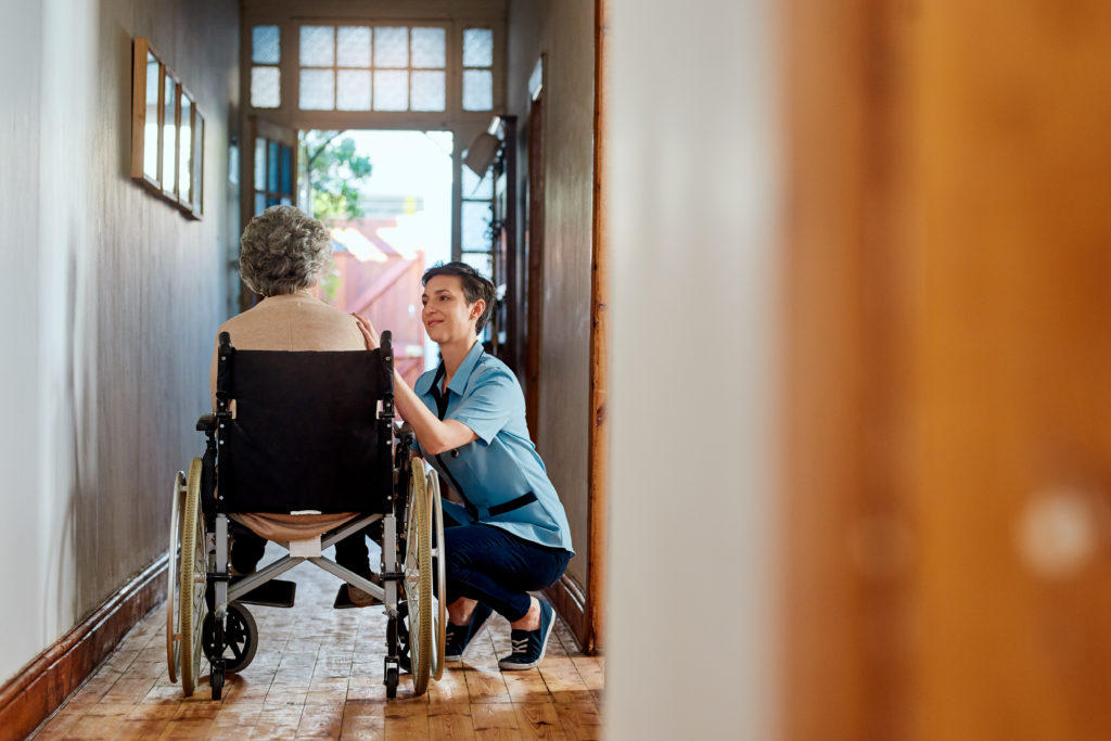A long corridor with an elderly woman in a wheelchair and a younger woman kneeling next to her in conversation