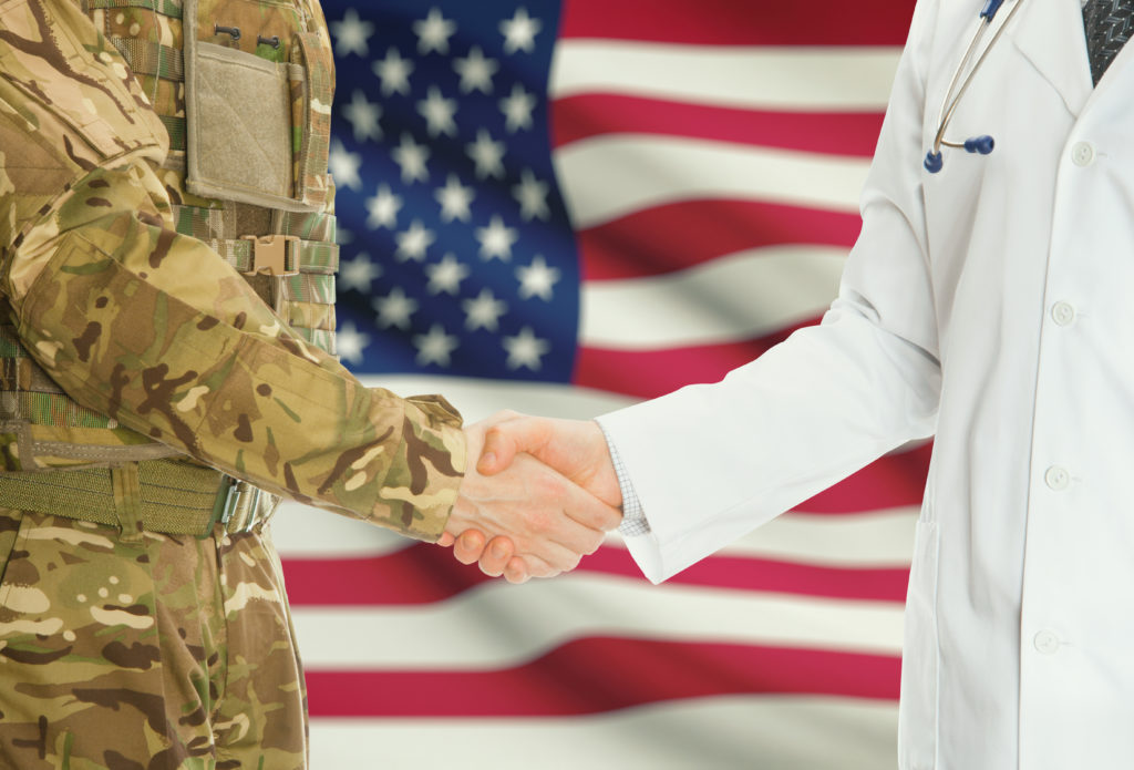 Military personnel shaking hands with medical professional with a US flag in the background