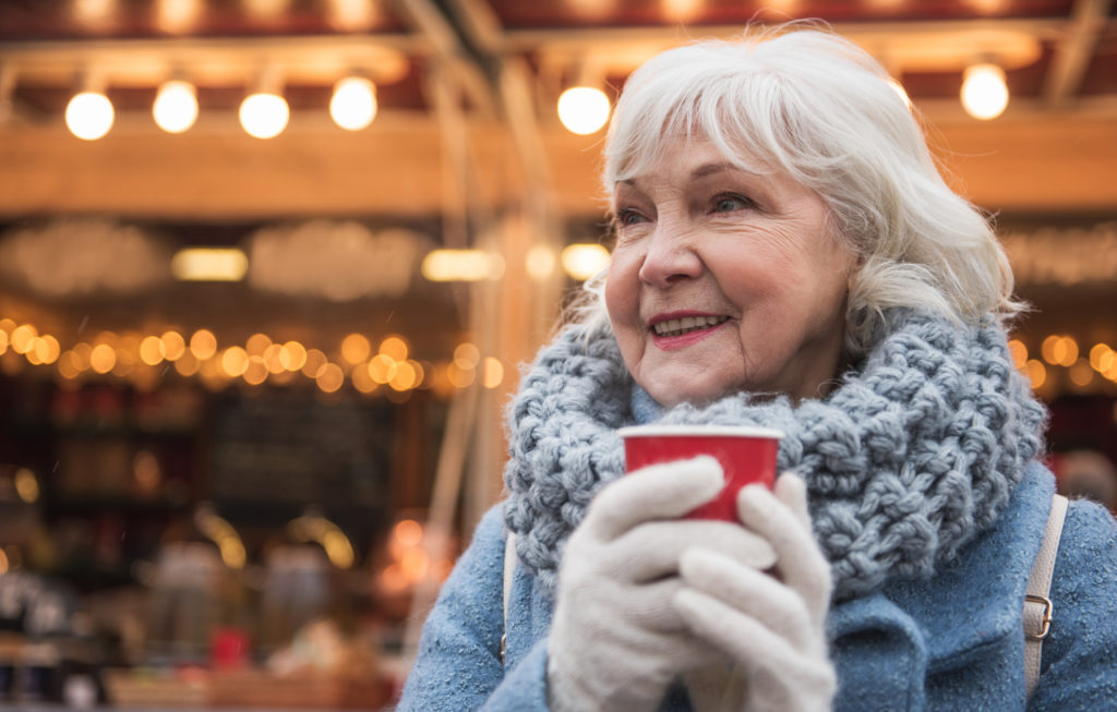 Enjoying winter holidays. Portrait of joyful senior woman drinking mulled wine with pleasure. She is standing on street and smiling. Copy space